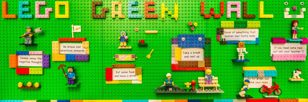 A green Lego wall spelling 'LEGO GREEN WALL' with minifigures and wellbeing prompts